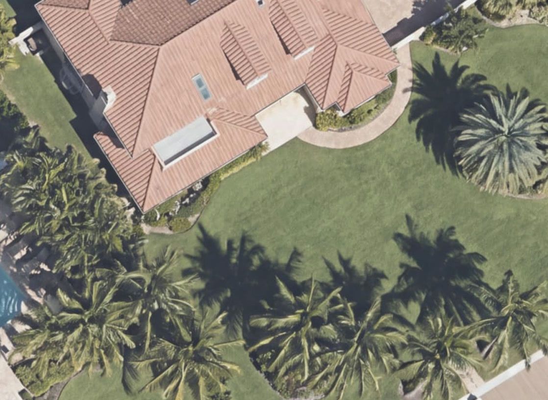 Satellite view of an estate home with a large open lawn and palm trees
